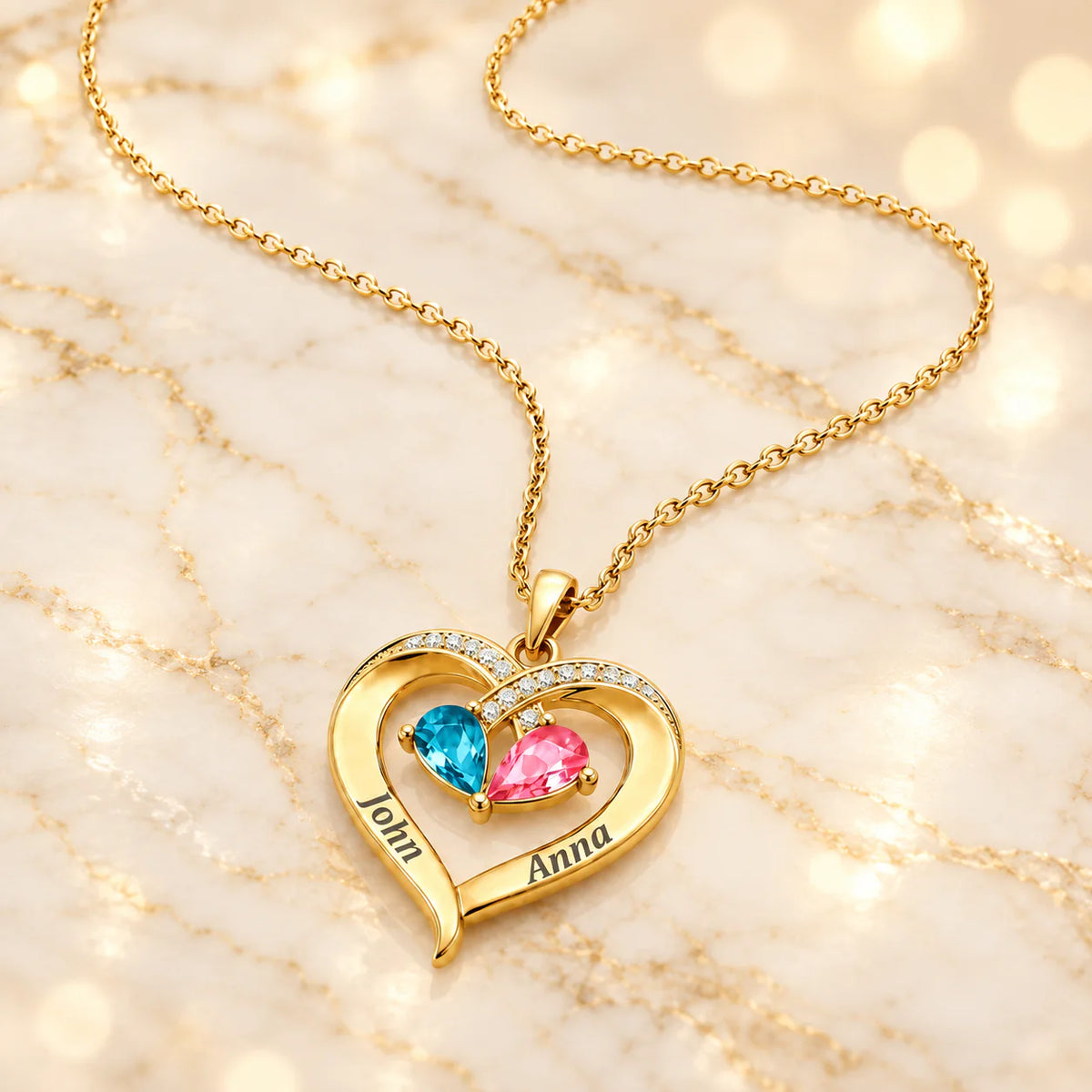 Gelbgold-Herzanhänger mit blauem und rosa Geburtsstein und Gravur John und Anna an feiner Kette auf hellem Marmor