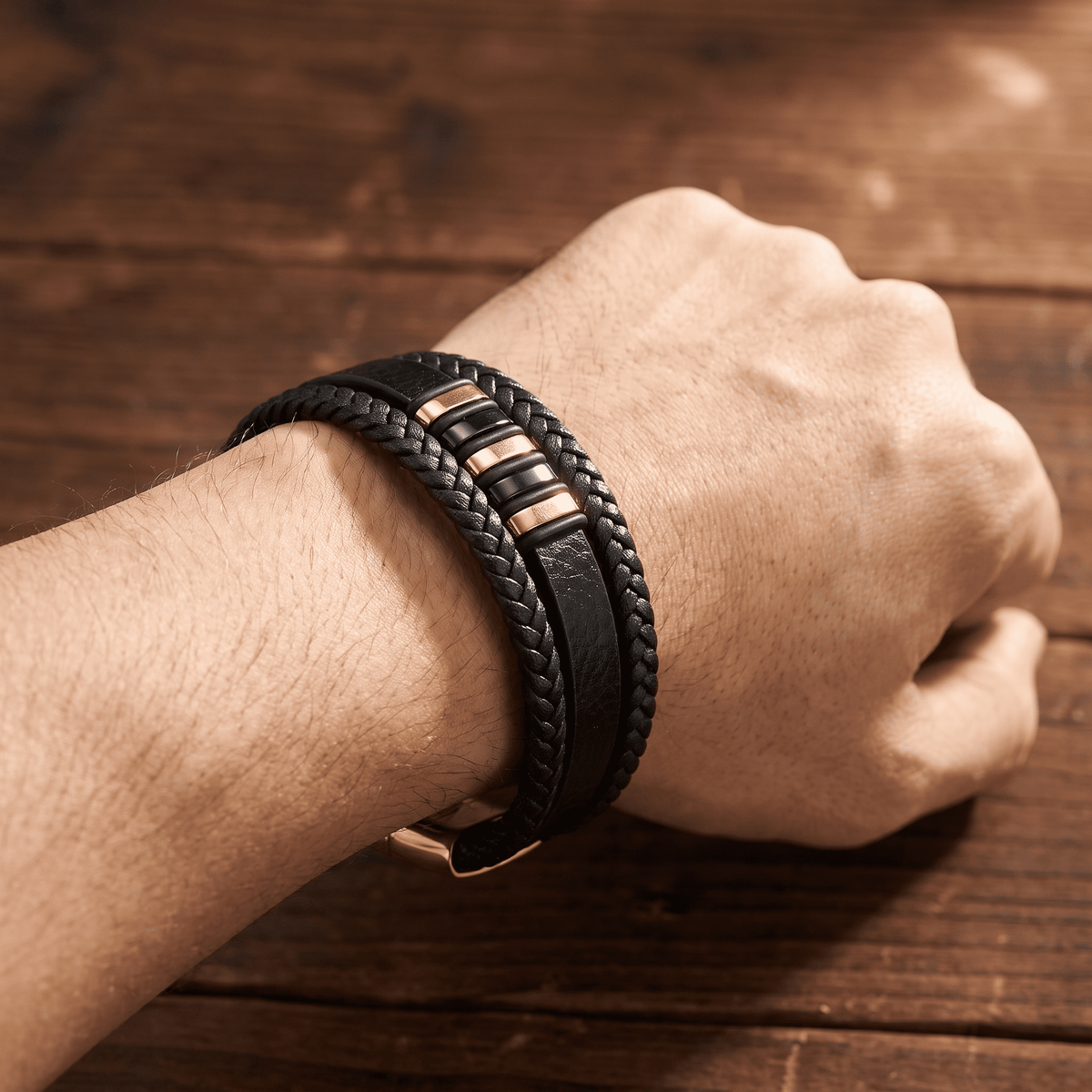 Geflochtenes Lederarmband mit Roségold-Detail am Handgelenk einer geballten Faust auf Holztisch