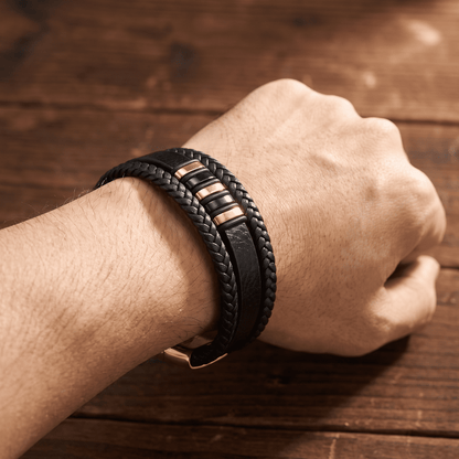 Geflochtenes Lederarmband mit Roségold-Detail am Handgelenk einer geballten Faust auf Holztisch