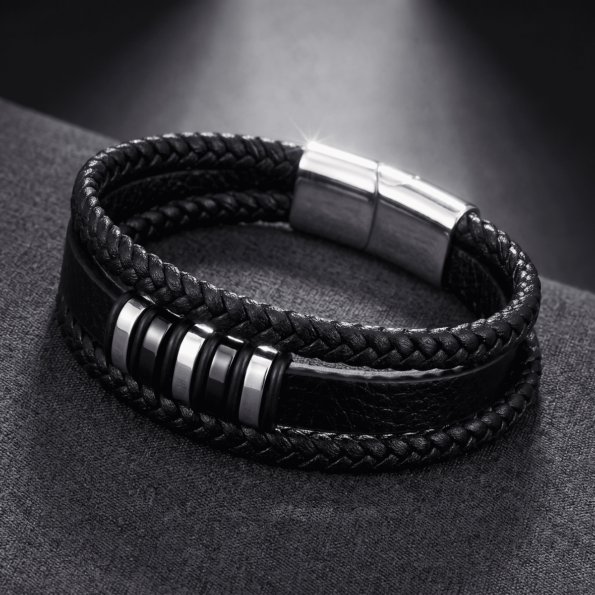 Lederarmband mit Silberverschluss und schwarzen Zwischenringen, Nahaufnahme vor dunklem Stoffhintergrund