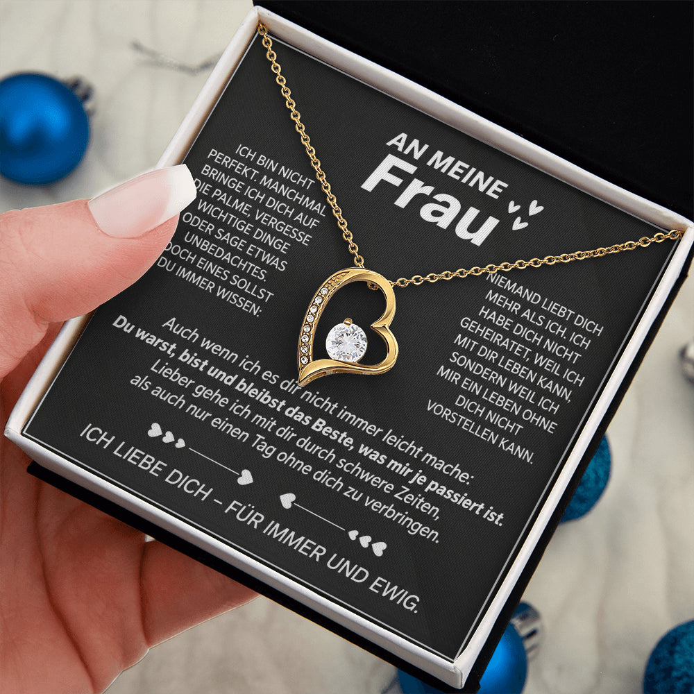 Hand hält die geöffnete Premium Box mit Gelbgold-Herzanhänger auf der Karte An meine Frau, blaue Kugeln im Hintergrund