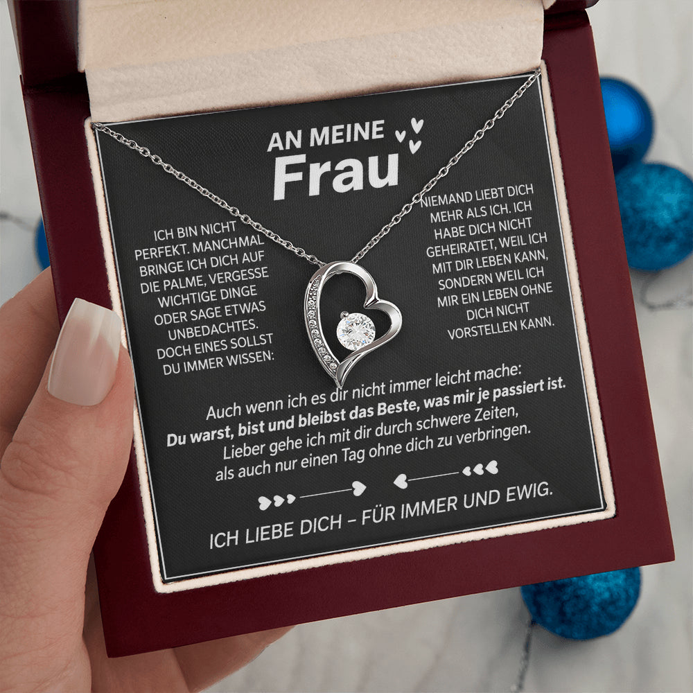 Hand hält die geöffnete Mahagoni-Box mit Weißgold-Herzanhänger auf der Karte An meine Frau, blaue Kugeln im Hintergrund
