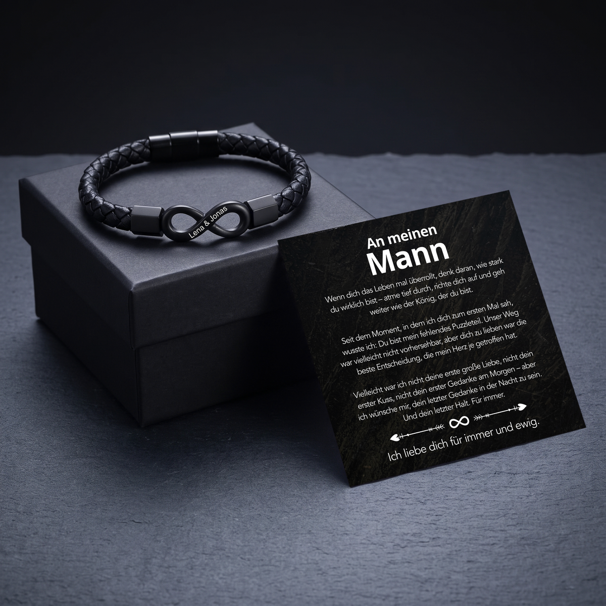 Armband mit schwarzem Infinity-Anhänger liegt auf kleiner grauer Geschenkbox, Botschaftskarte An meinen Mann lehnt daran