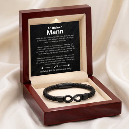 Braune Holzgeschenkbox auf weißem Seidenstoff, geöffnet mit Botschaftskarte und Armband mit schwarzem Infinity-Anhänger