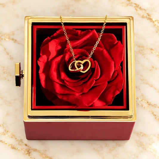Rote Rosenbox mit echter roter Rose und goldfarbener Halskette auf hellem Marmor