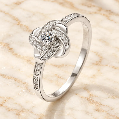 Weißgoldfarbener Knotenring mit Zirkonia und Mittelstein auf hellem Marmor