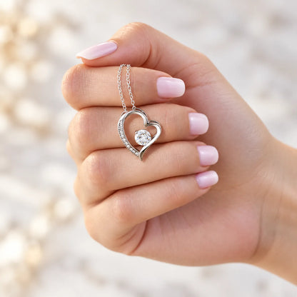Weißgold-Herzanhänger an einer Hand vor hellem Hintergrund