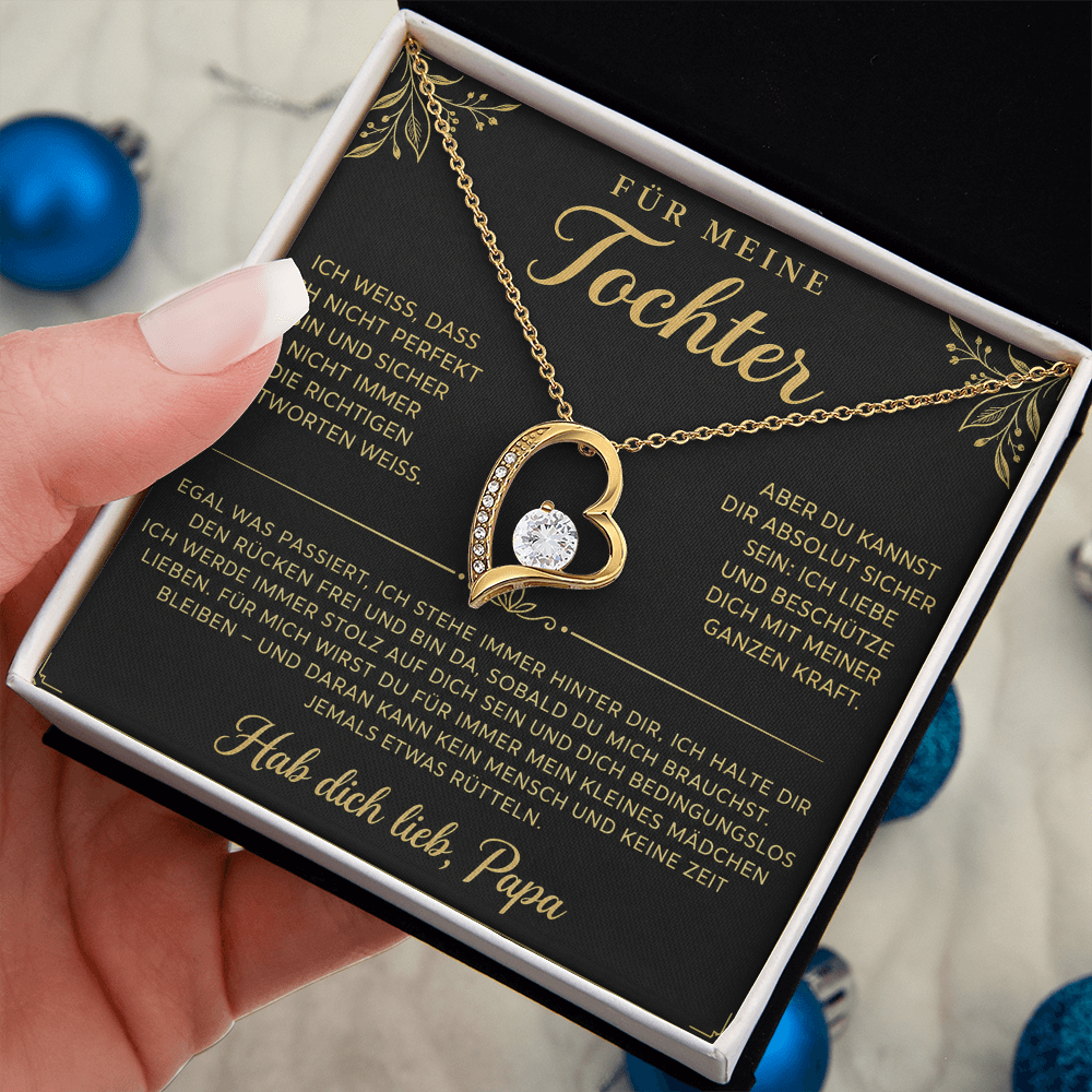 Hand hält die geöffnete Box mit goldenem Herzanhänger auf der Papa-Karte, blaue Weihnachtskugeln im Hintergrund
