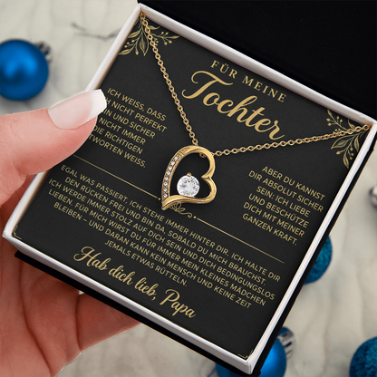 Hand hält die geöffnete Box mit goldenem Herzanhänger auf der Papa-Karte, blaue Weihnachtskugeln im Hintergrund