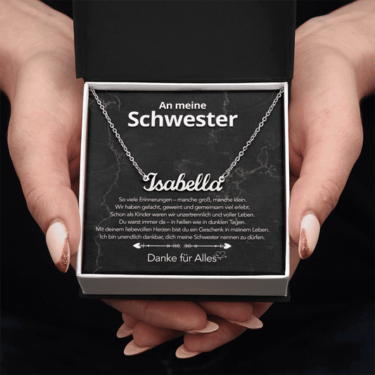Weißgold-Namenskette Isabella auf Karte An meine Schwester in schwarzer Box, von zwei Händen gehalten